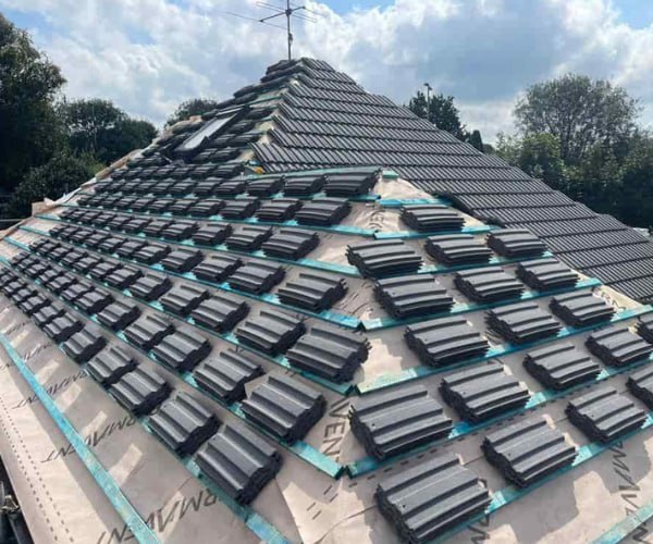 This is a photo of a new hip roof being installed. New felt, battens, and grey tiles have been installed, also a new velux window. Works carried out by STW Roofing Flitwick