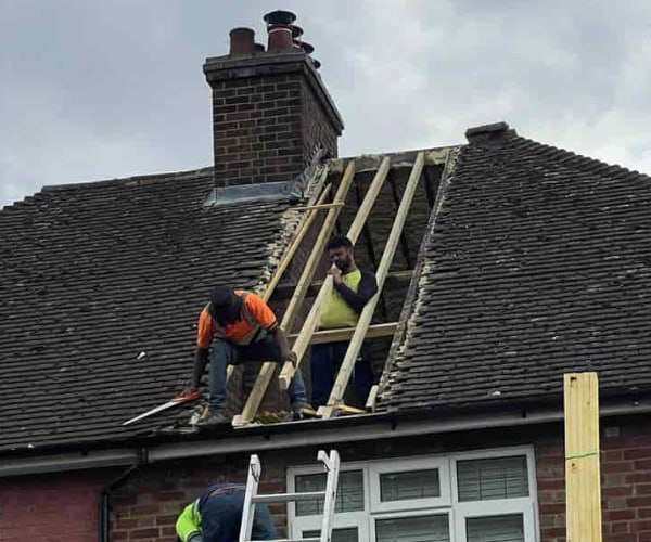 This is a photo of a roof repair being carried out. A section of the roof has been stripped and two roofers are replacing the rafters. Works being carried out by STW Roofing Flitwick